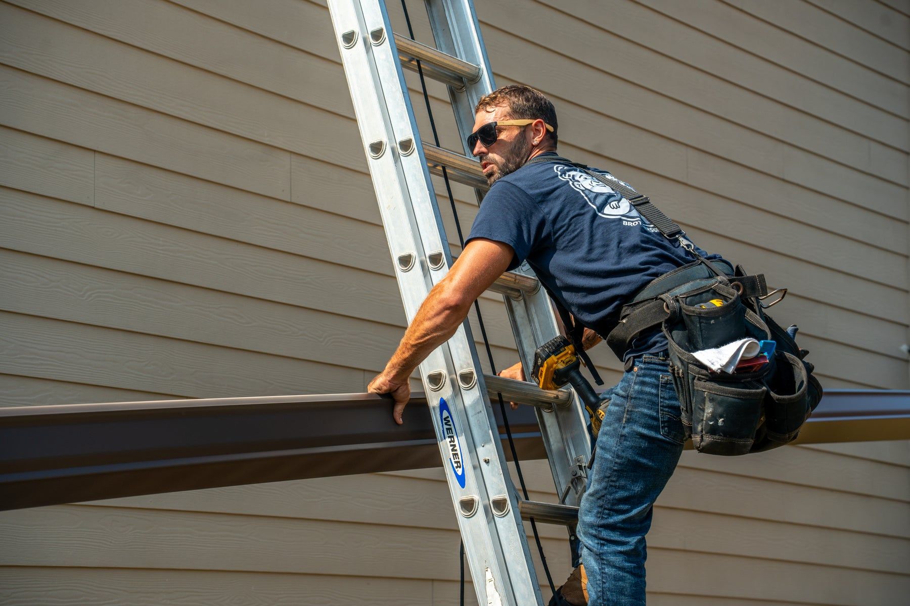 Installer carrying a gutter section up the ladder