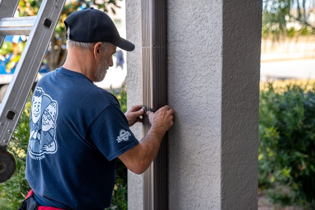 Installer securing a downspout to a stucco wall